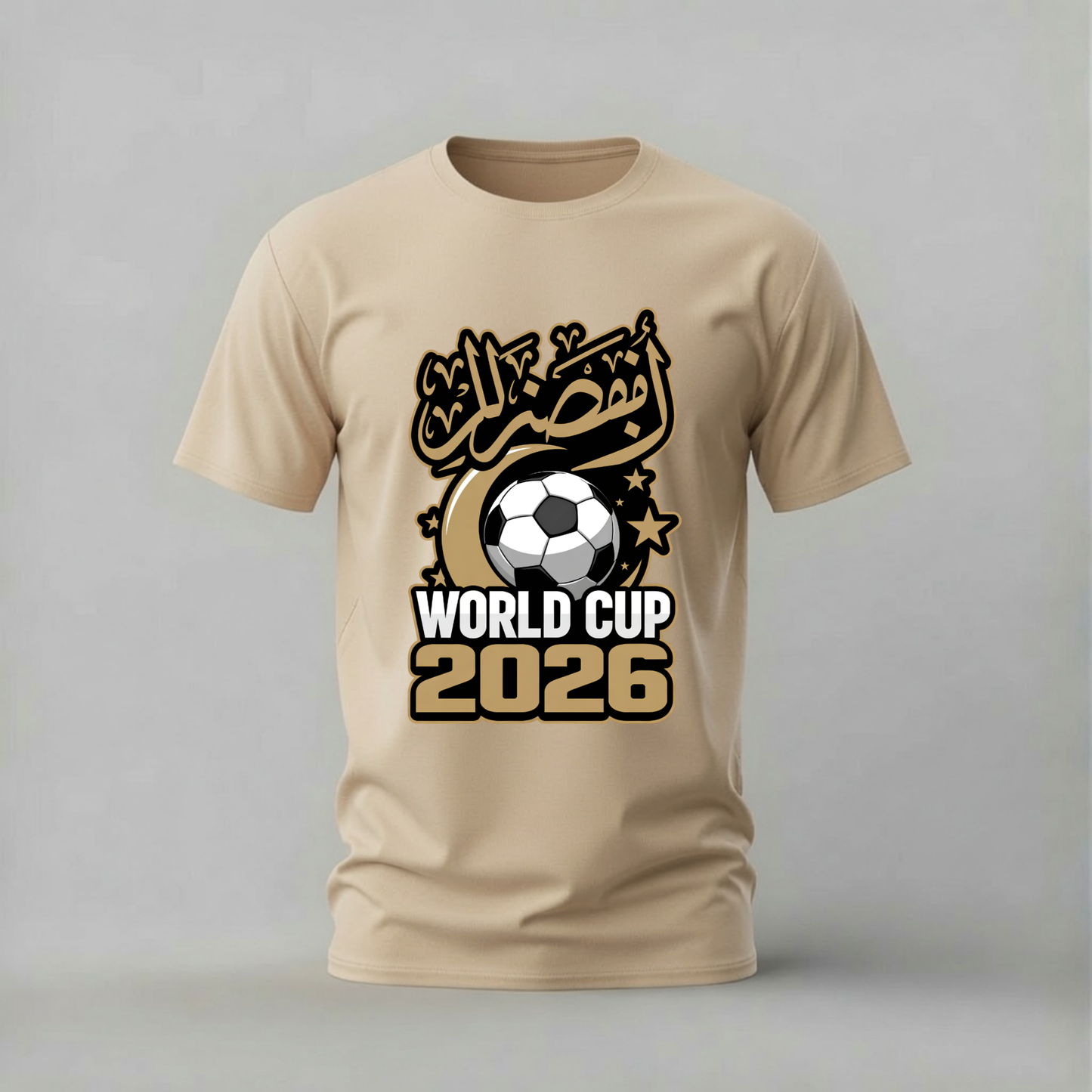 A beige short-sleeve crewneck t-shirt featuring a graphic design for the 2026 World Cup. The design includes Arabic calligraphy, a soccer ball, stars, and the text 'WORLD CUP 2026' in white and gold.
