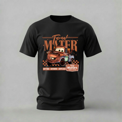 A black short-sleeve crewneck t-shirt featuring a graphic print of the character Mater from Disney's Cars, with retro-style text reading 'Tow Mater' and 'Anytime - Anywhere - Anyplace' on a light gray background.