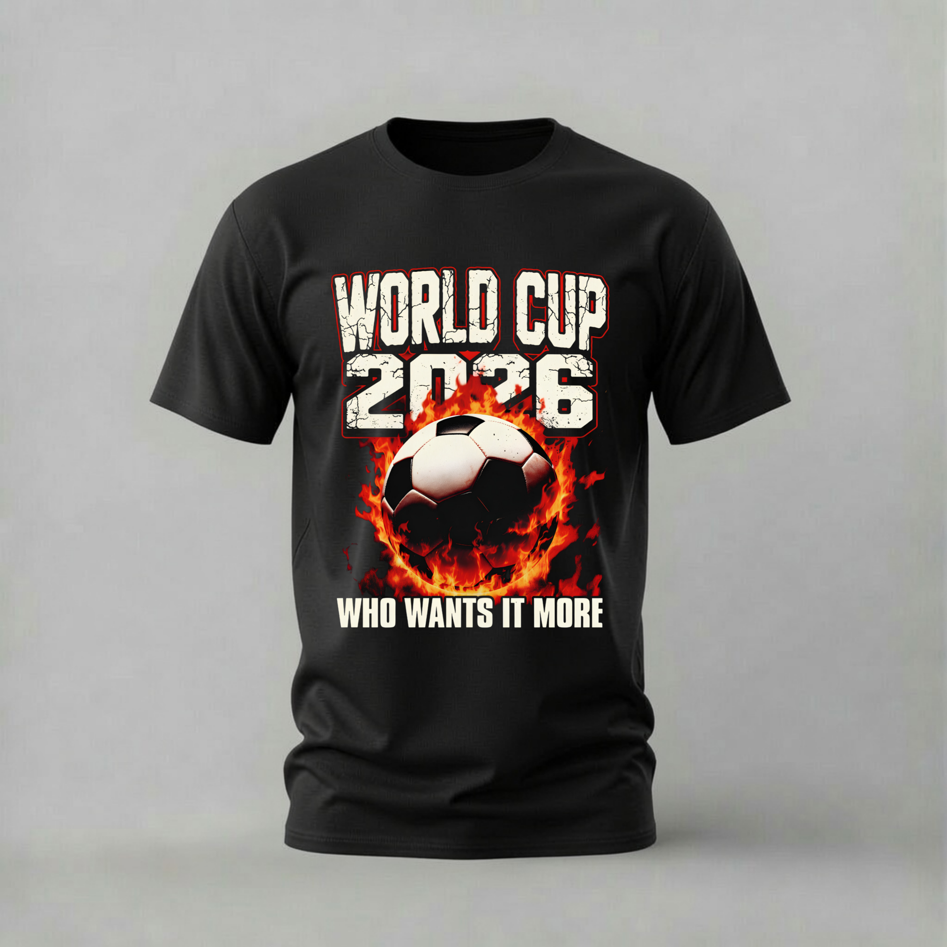 A black short-sleeve t-shirt with a graphic print of a soccer ball engulfed in flames, with the text 'WORLD CUP 2036' above and 'WHO WANTS IT MORE' below, displayed on a neutral gray background.