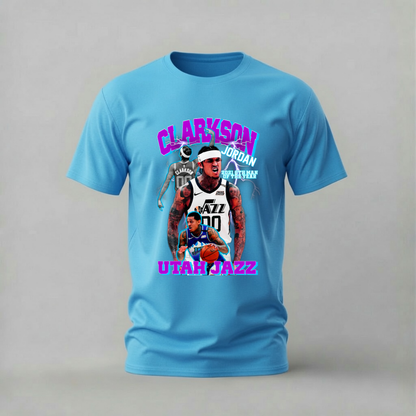 A light blue short-sleeve t-shirt with a colorful graphic print of basketball player Jordan Clarkson and the Utah Jazz, displayed on a neutral gray background.