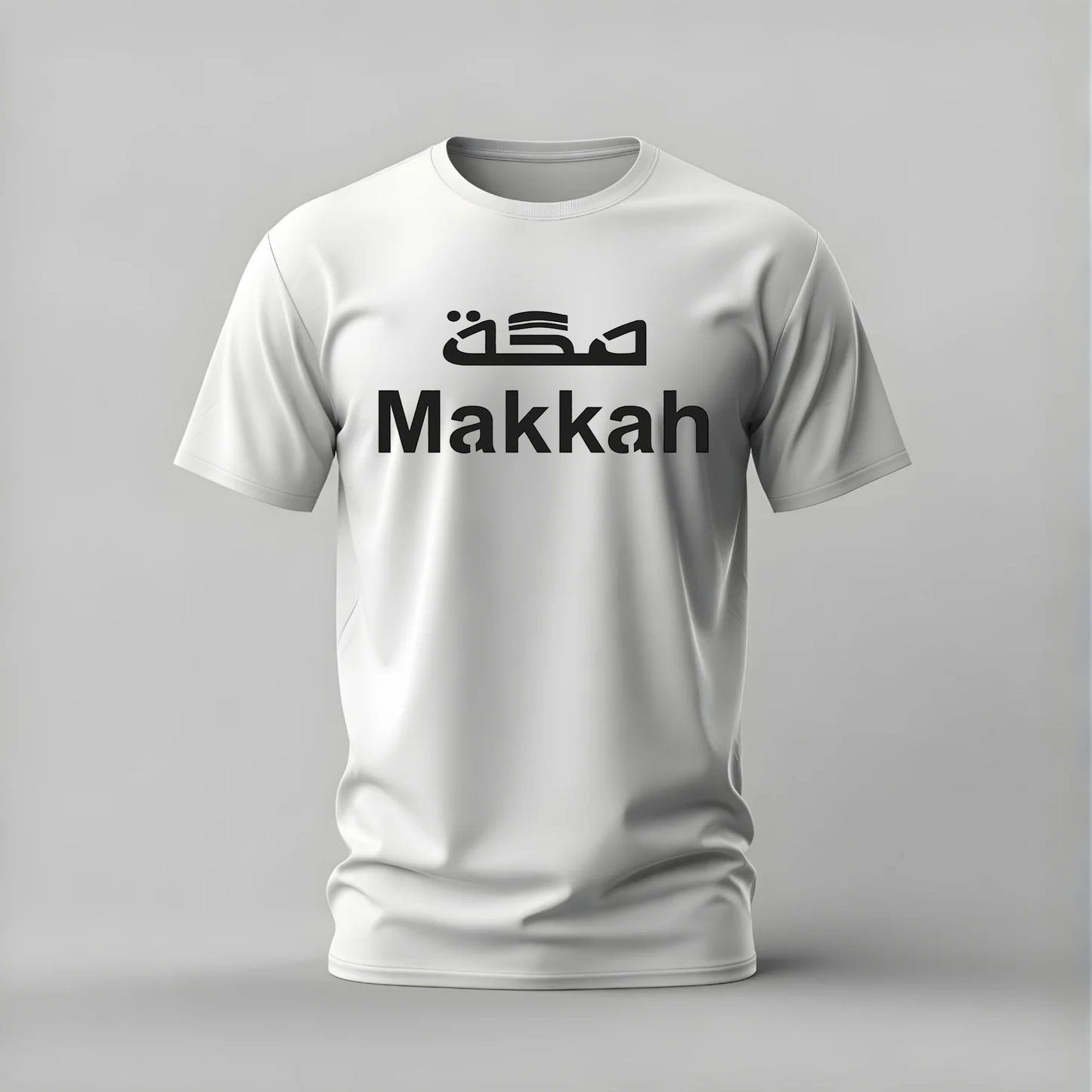 A white short-sleeve crewneck t-shirt with 'Makkah' printed in black across the chest, featuring stylized Arabic calligraphy above it, shown on a neutral gray background.