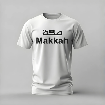 A white short-sleeve crewneck t-shirt with 'Makkah' printed in black across the chest, featuring stylized Arabic calligraphy above it, shown on a neutral gray background.