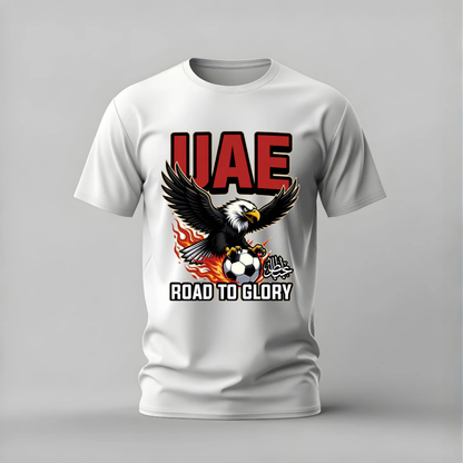 A white short-sleeve crewneck t-shirt with a graphic print on the front. The design features the text 'UAE' in bold red letters, an eagle clutching a soccer ball with flames, and the text 'ROAD TO GLORY' in white.